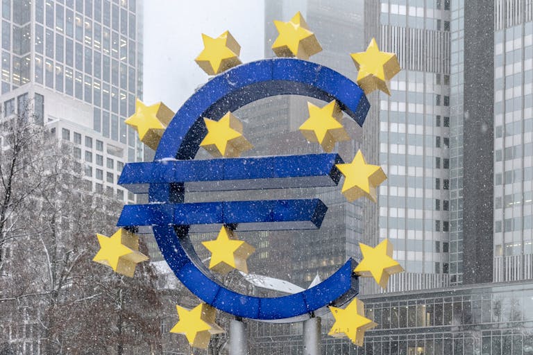A euro sign in front of tall buildings